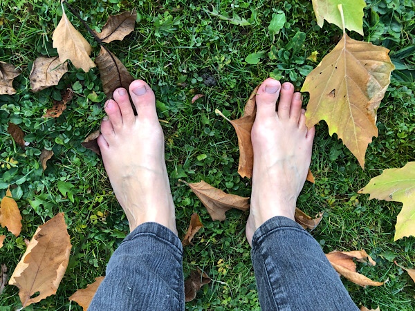 nackte Füße auf einer Wiese mit Herbstlaub