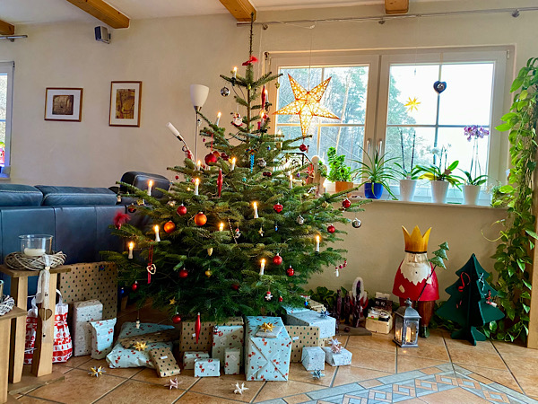 Ein festlich geschmückter Weihnachtsbaum in einem weihnachtlich dekorierten Zimmer, darunter liegen Geschenke