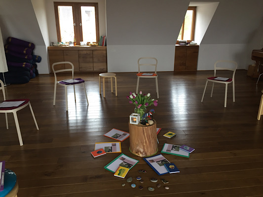 Seminarraum mit einigen Stühlen; in der Mitte stehen Blumen auf einem Holzklotz, drum herum sind Hefte angeordnet
